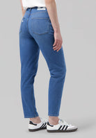 Person wearing eco-friendly MUD Jeans made from organic cotton, showcasing medium blue denim with white casual sneakers.