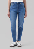 High-waisted, slim-fit blue jeans made of organic cotton, paired with white sneakers, worn by a model in a casual pose.
