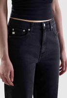 Black high-waisted jeans made from sustainable denim, worn with a sleeveless ribbed black top, close-up view.