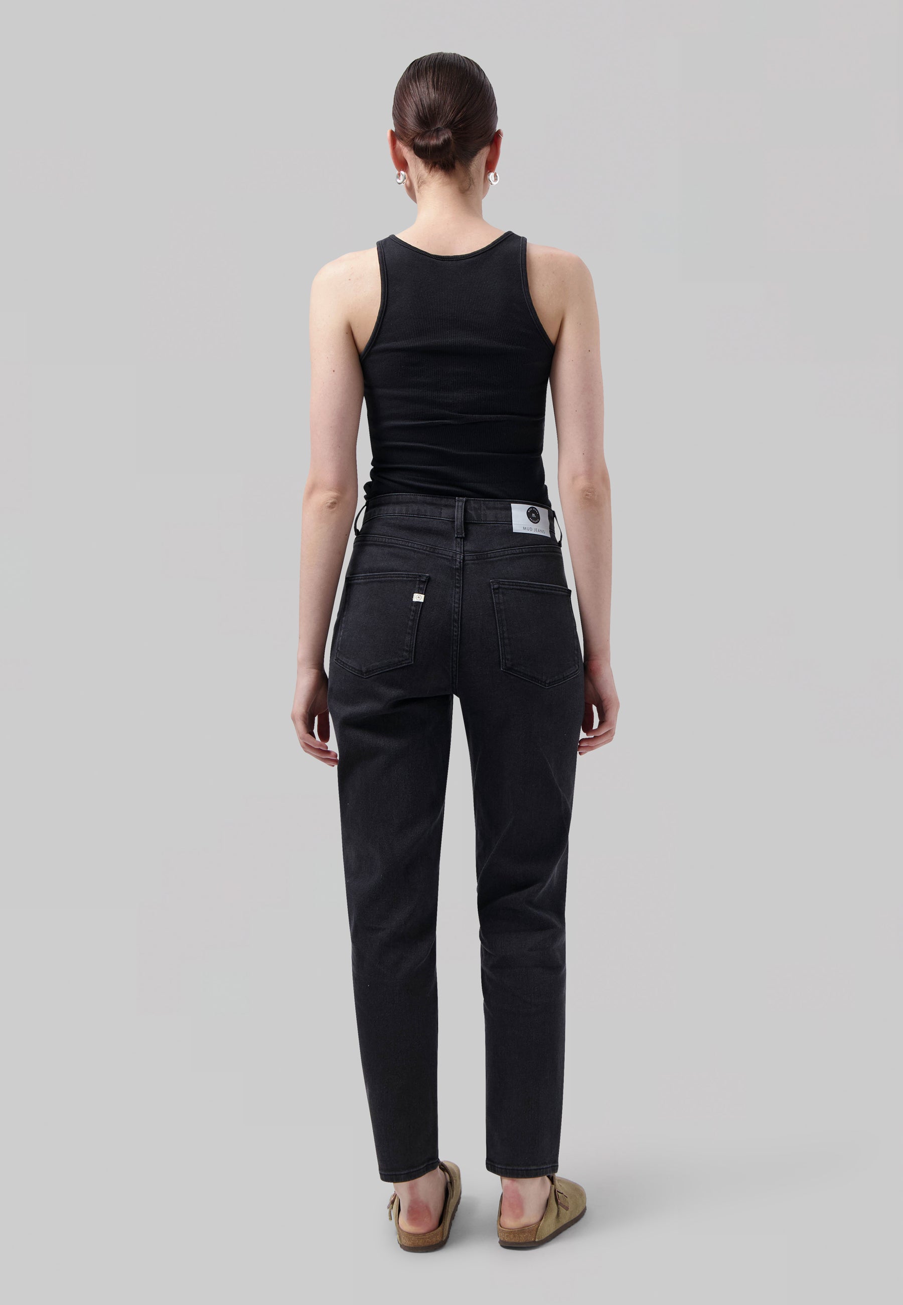 Woman wearing black ribbed tank top and charcoal straight-leg jeans with a back label, styled with tan slip-on shoes.