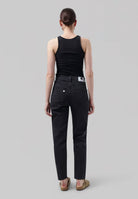 Woman wearing black ribbed tank top and charcoal straight-leg jeans with a back label, styled with tan slip-on shoes.