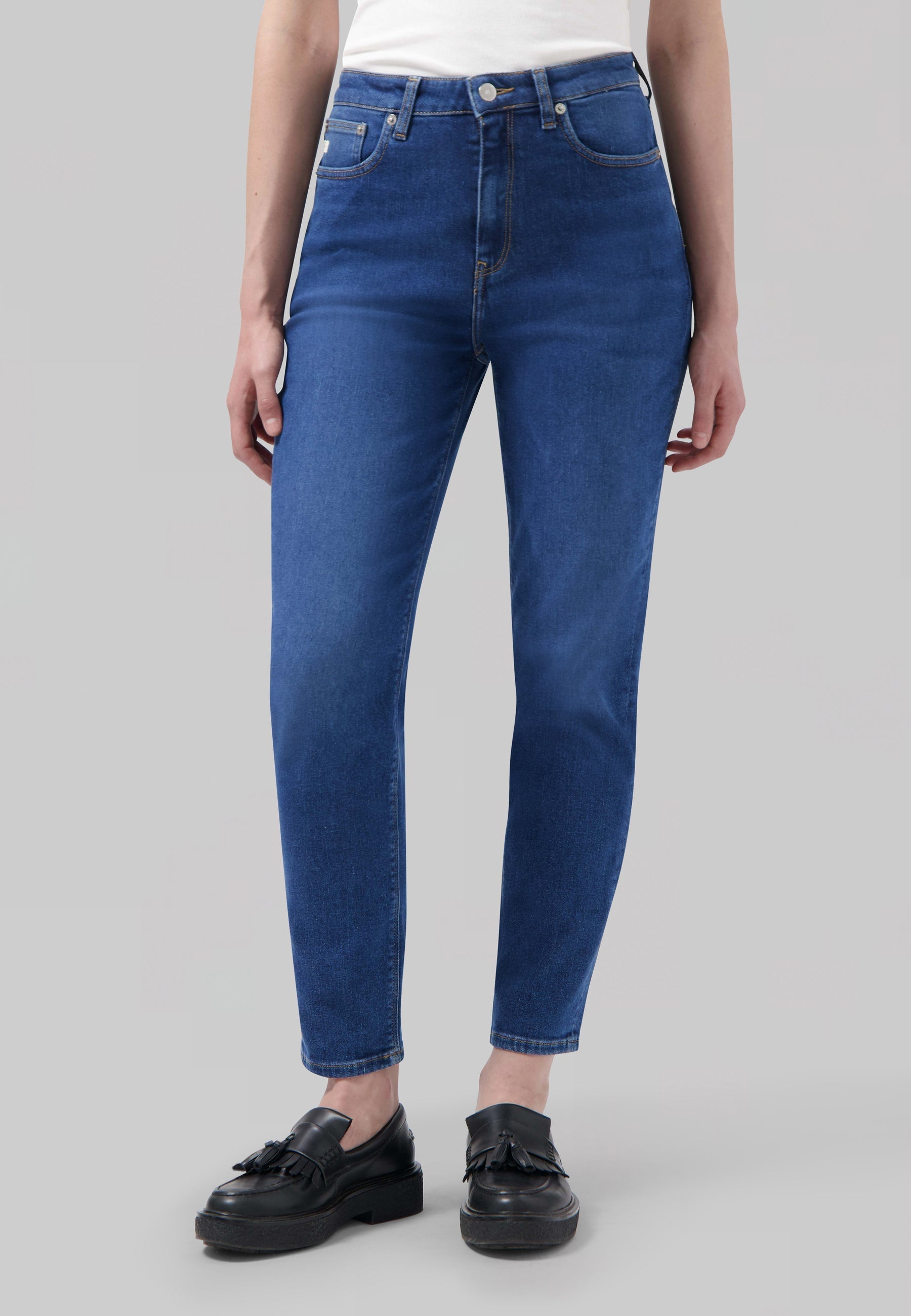 A person wearing classic blue high-waisted jeans with a plain white top and black tassel loafers, showcasing casual style.