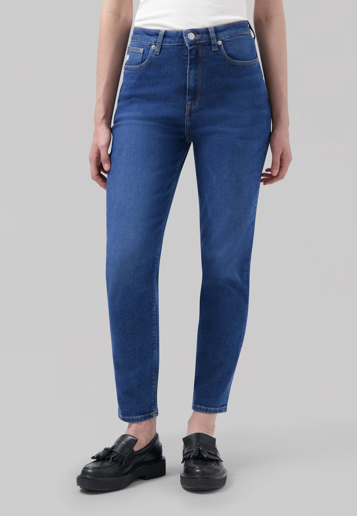A person wearing classic blue high-waisted jeans with a plain white top and black tassel loafers, showcasing casual style.
