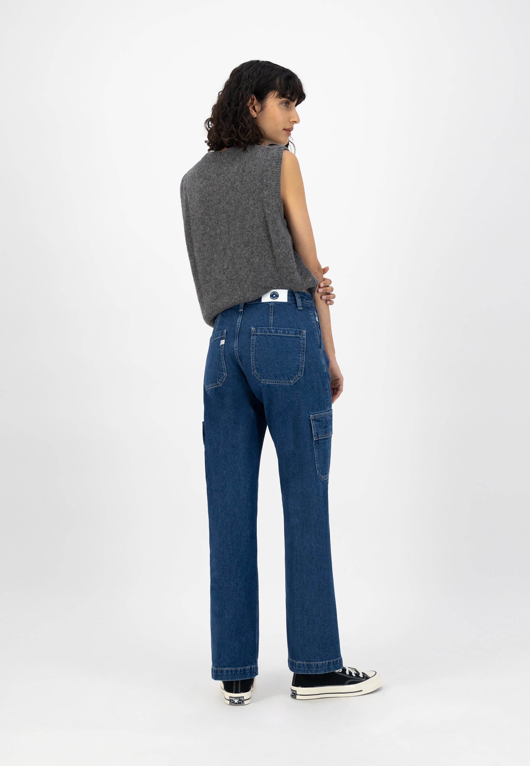 A woman wearing a sleeveless gray woolen top and blue denim jeans with a relaxed fit, styled with black sneakers.