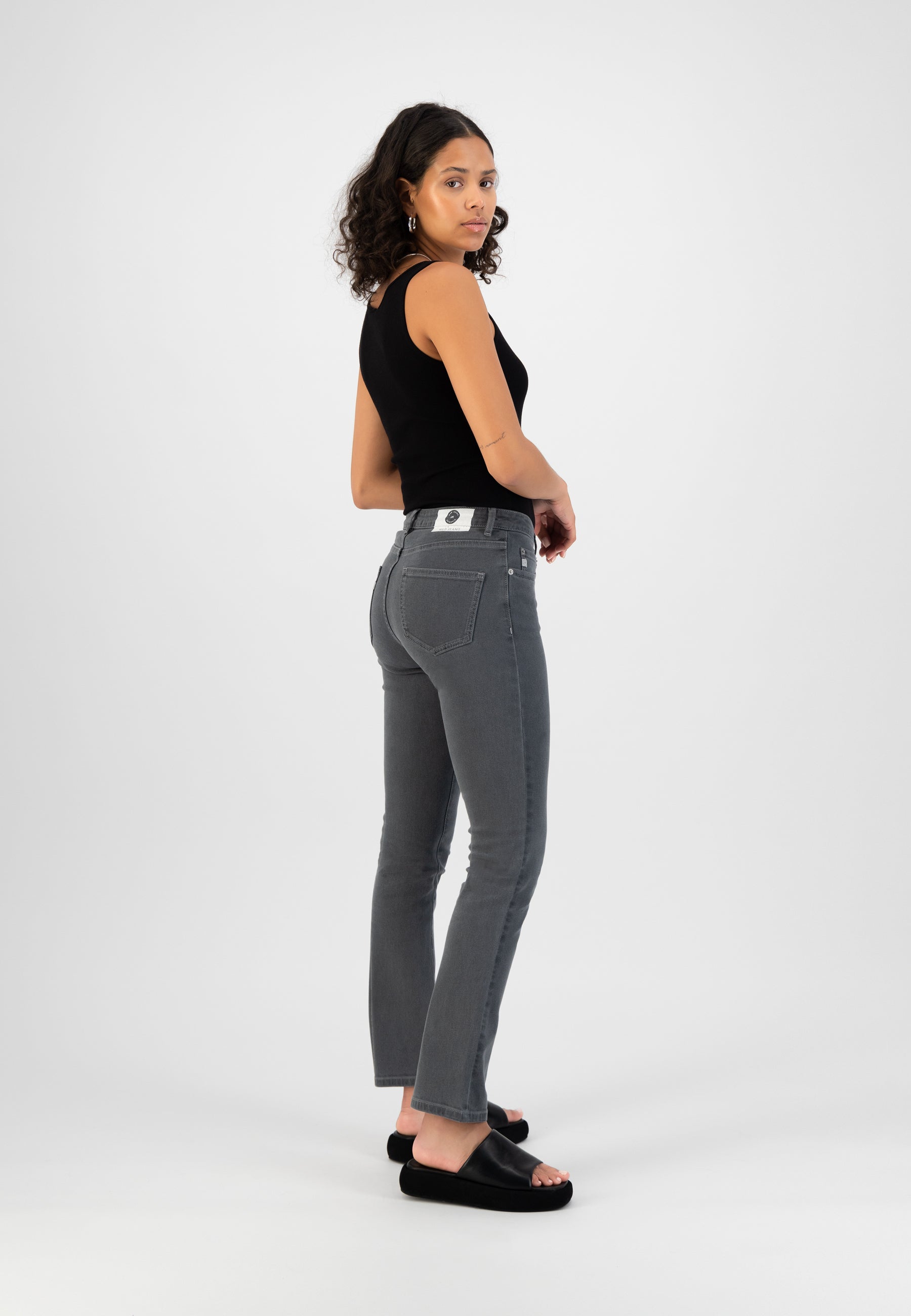 Gray stretch denim jeans paired with a black sleeveless top, showcasing a casual yet stylish look with black slip-ons.