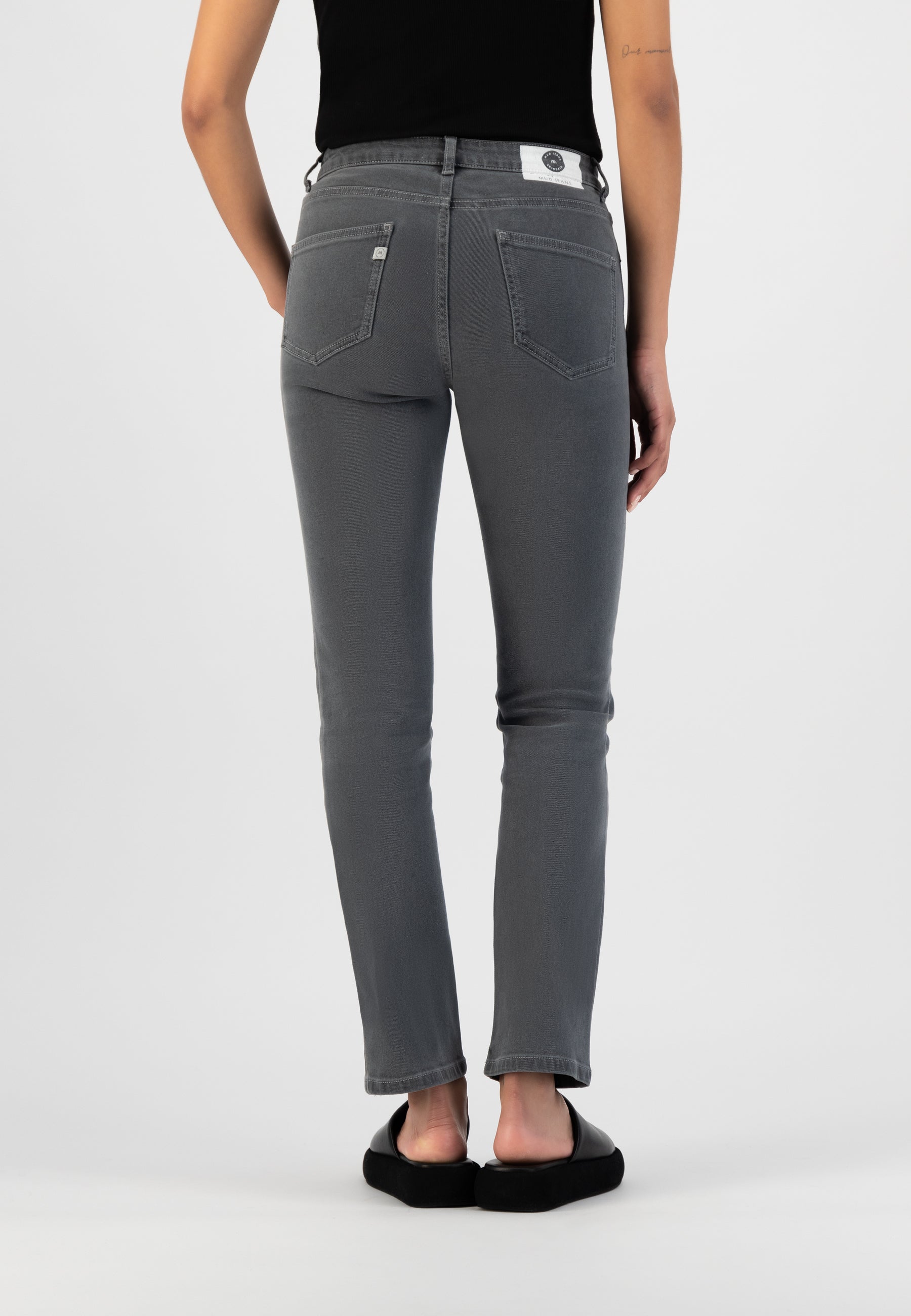Mid-rise, slim-fit jeans in charcoal gray, showcasing a back view, paired with a black sleeveless top and black slip-on shoes.