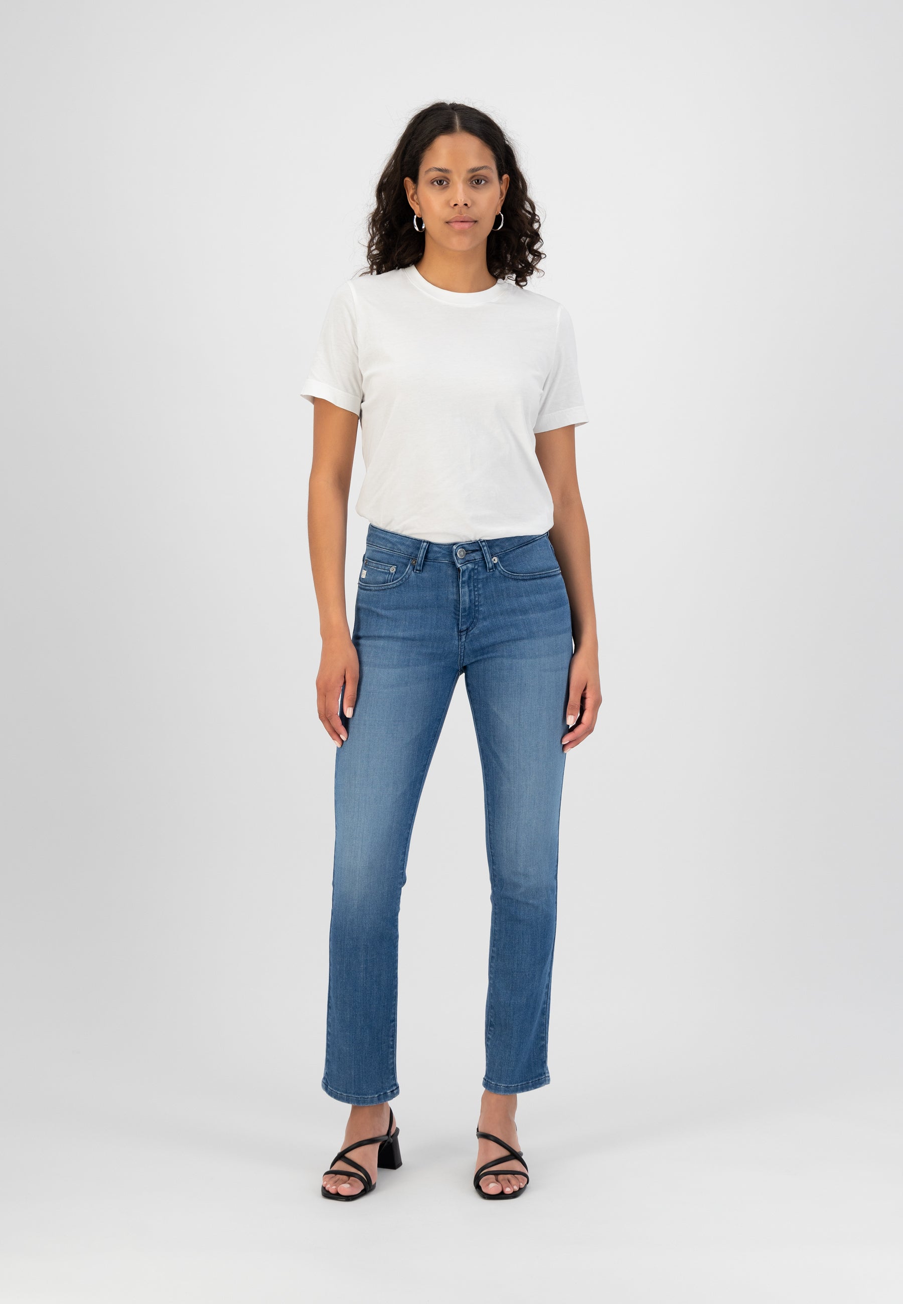 A woman wearing light blue straight-leg jeans paired with a plain white t-shirt and black strappy sandals.