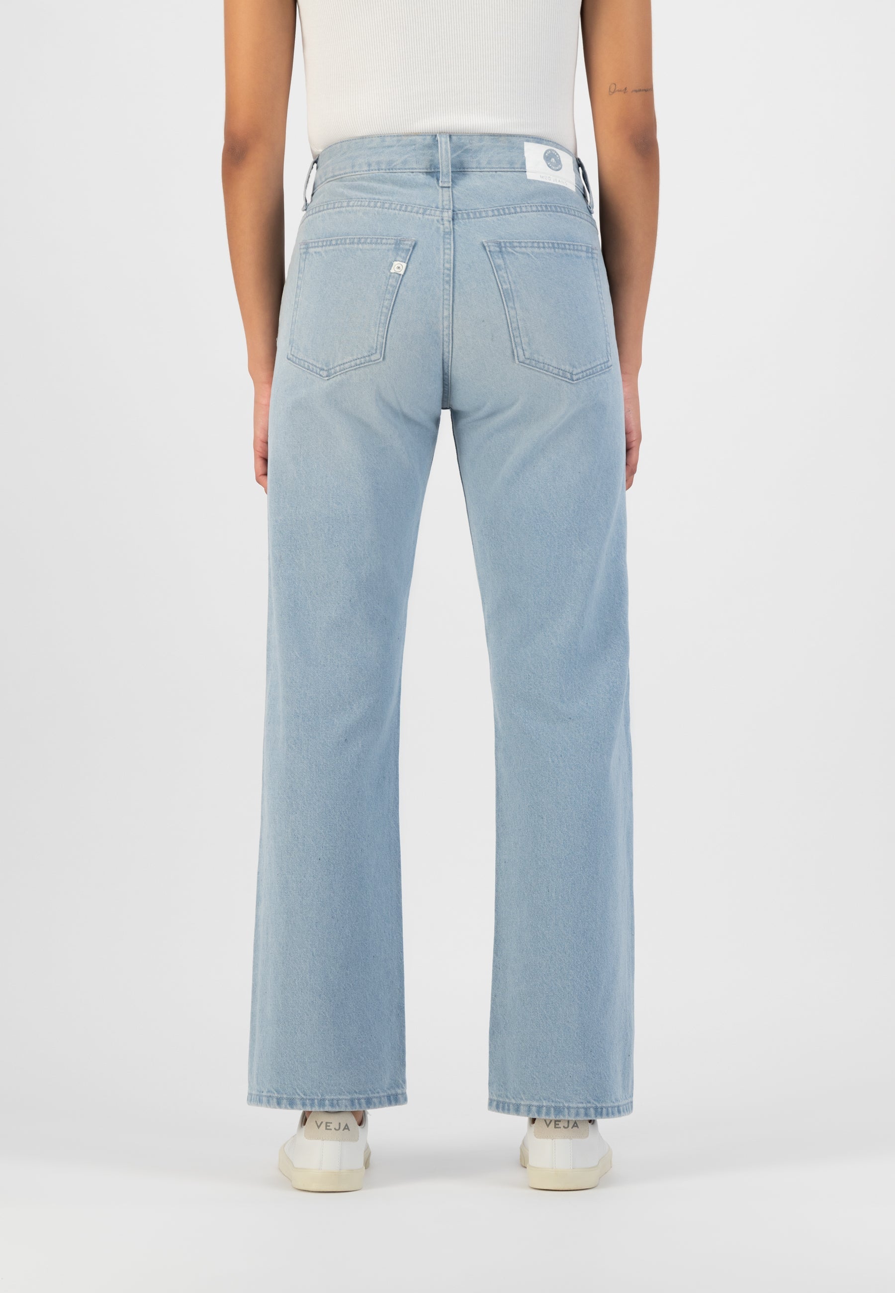High-waisted light blue jeans made from organic cotton, showing the back view paired with a sleeveless white top.