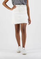 White denim mini skirt with frayed hem, paired with a gray top and white sneakers, showcasing a casual fashion style.