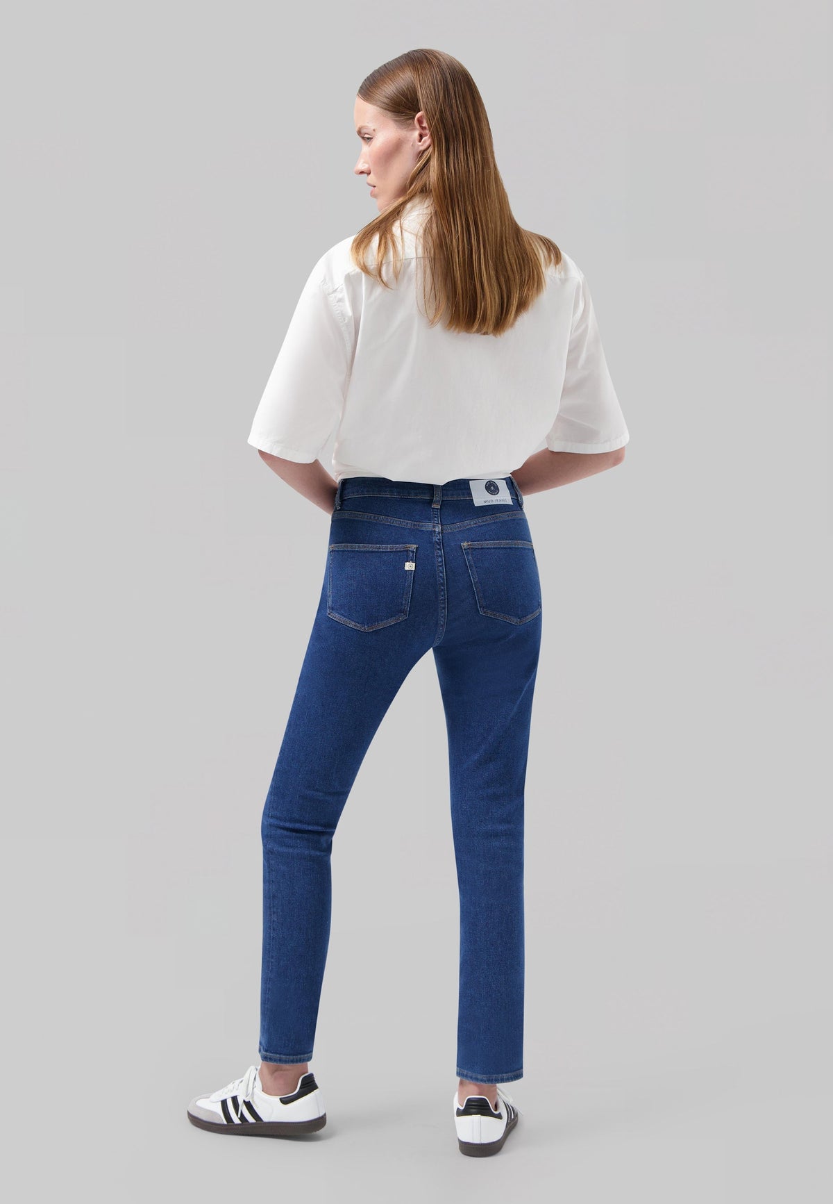 Woman wearing classic blue jeans and white short-sleeve shirt viewed from behind, highlighting stylish casual attire.
