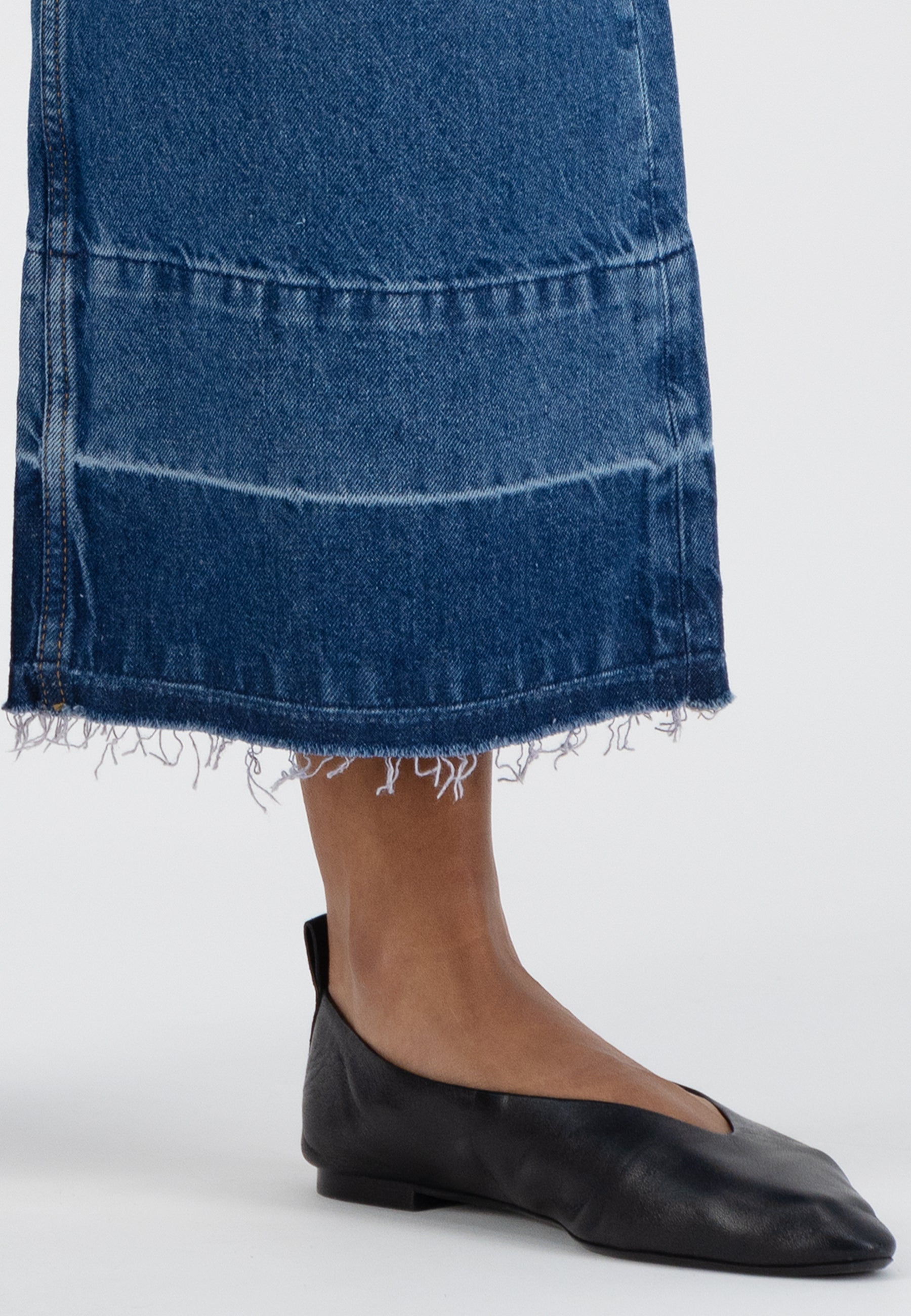 Frayed hem blue denim skirt paired with black leather flats on a neutral background, showcasing casual fashion style.