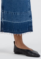 Frayed hem blue denim skirt paired with black leather flats on a neutral background, showcasing casual fashion style.