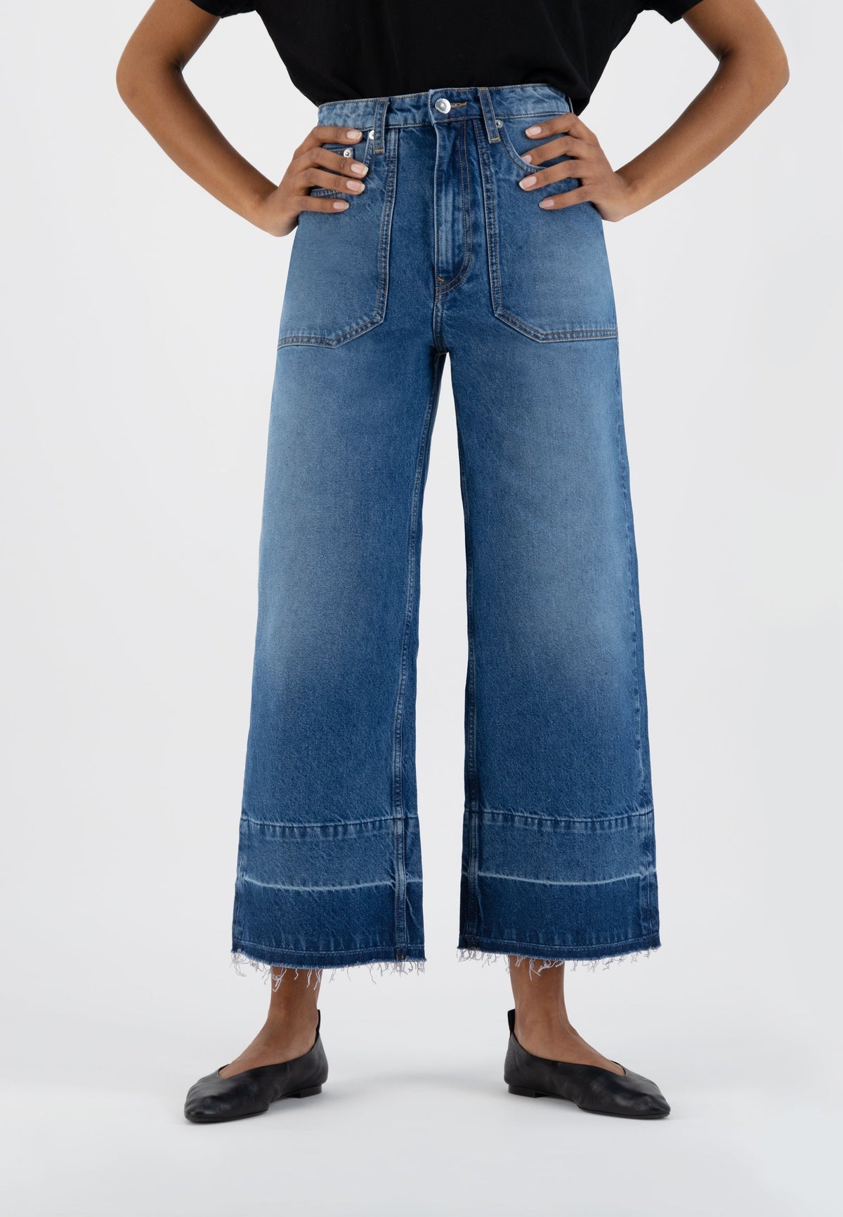 High-waisted wide-leg denim jeans in medium blue with front pockets, worn with a black top and flat black shoes.