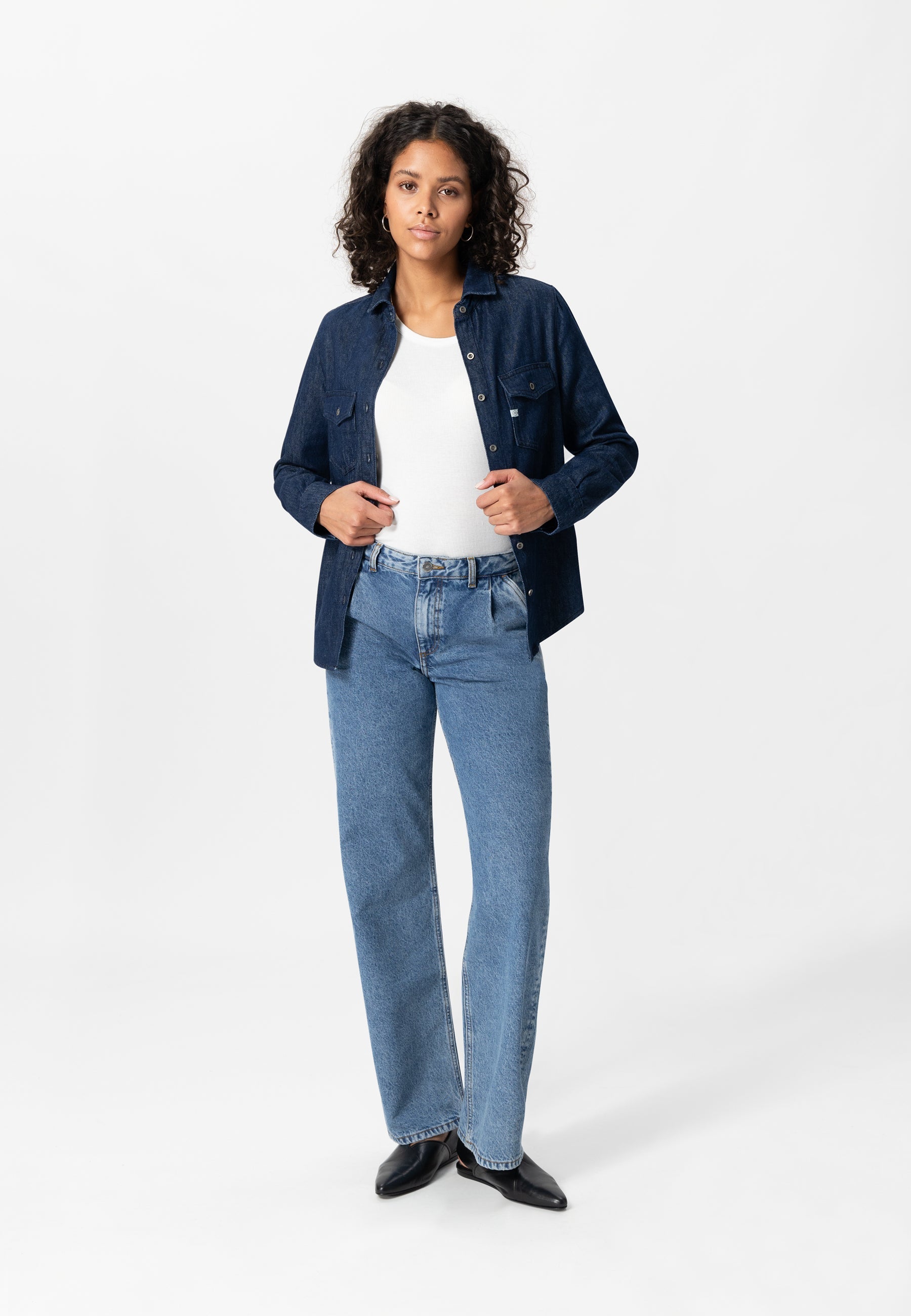 Casual outfit featuring a white tank top with a dark blue denim jacket and light blue straight-leg jeans, styled with black shoes.