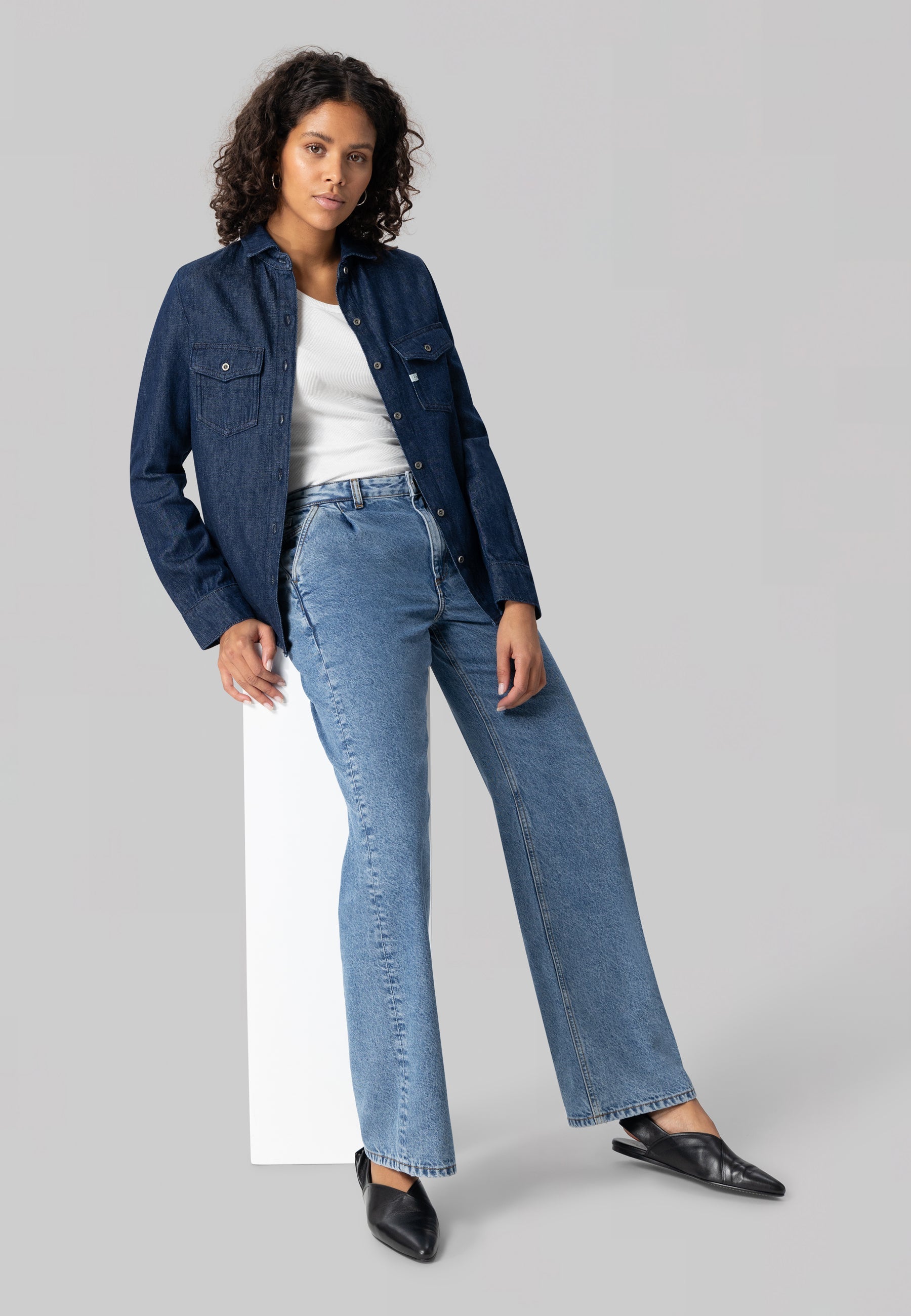 Model wearing a dark blue denim jacket over a white top, paired with light blue high-waisted jeans and black shoes.