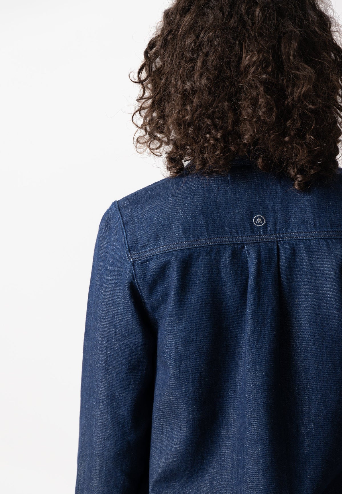 Close-up of a denim jacket, dark blue and sustainably made, showing detailed stitching and elegant design on the back.