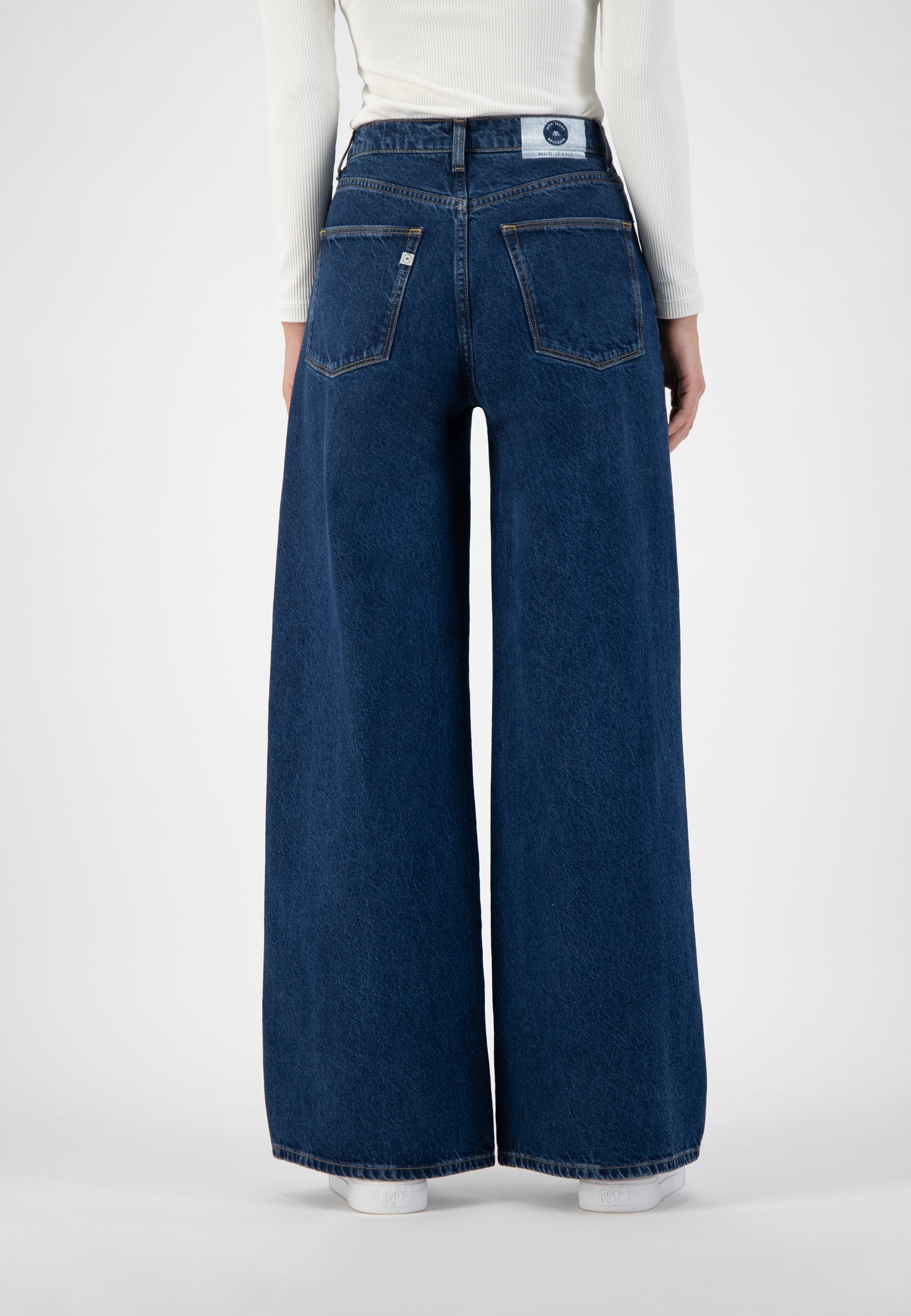 Wide-leg blue denim jeans with high waist, showcasing rear pockets, worn with a white ribbed long-sleeve top.
