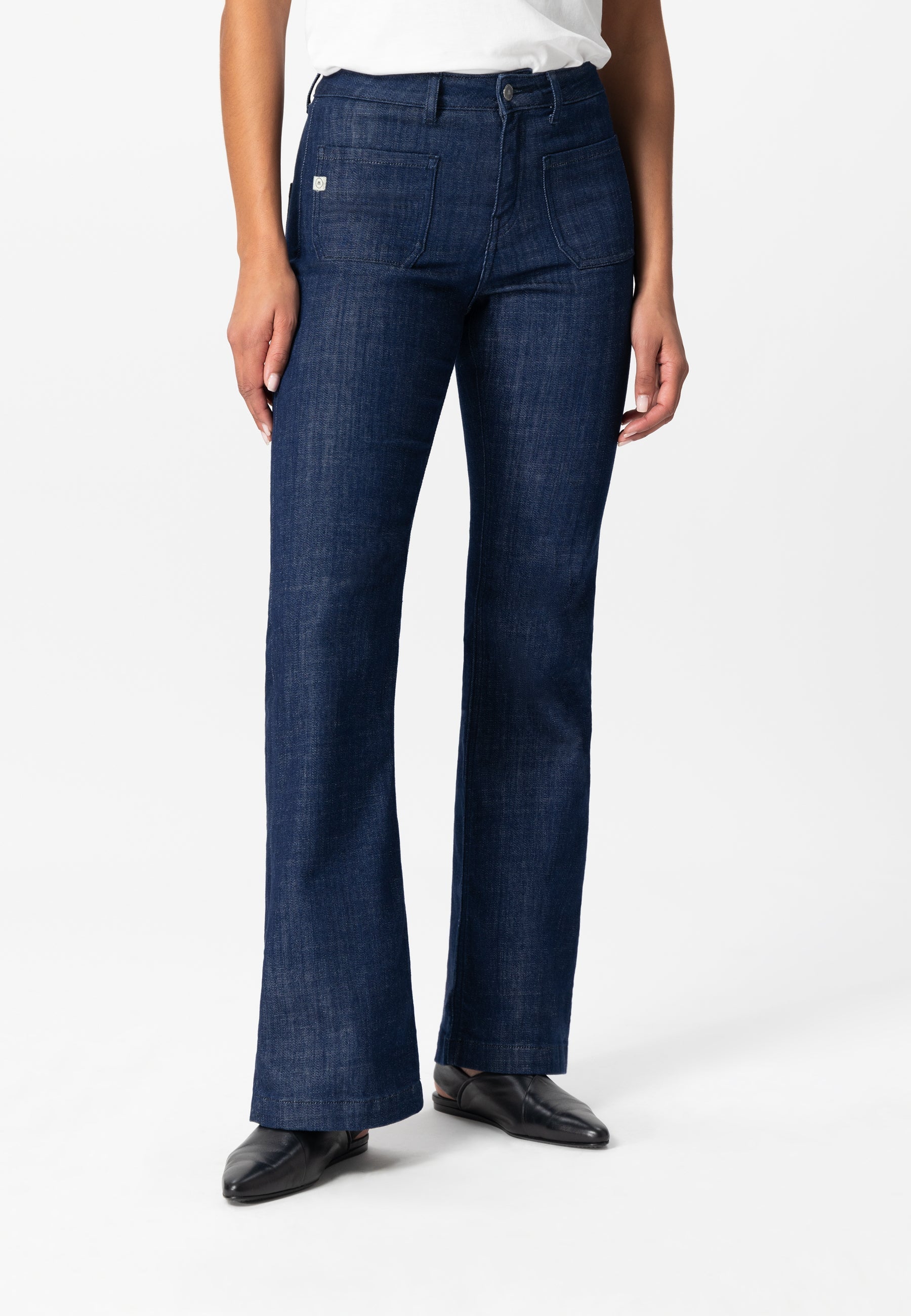 Dark blue bootcut jeans made from sustainable denim, worn with a casual white top and black leather shoes.