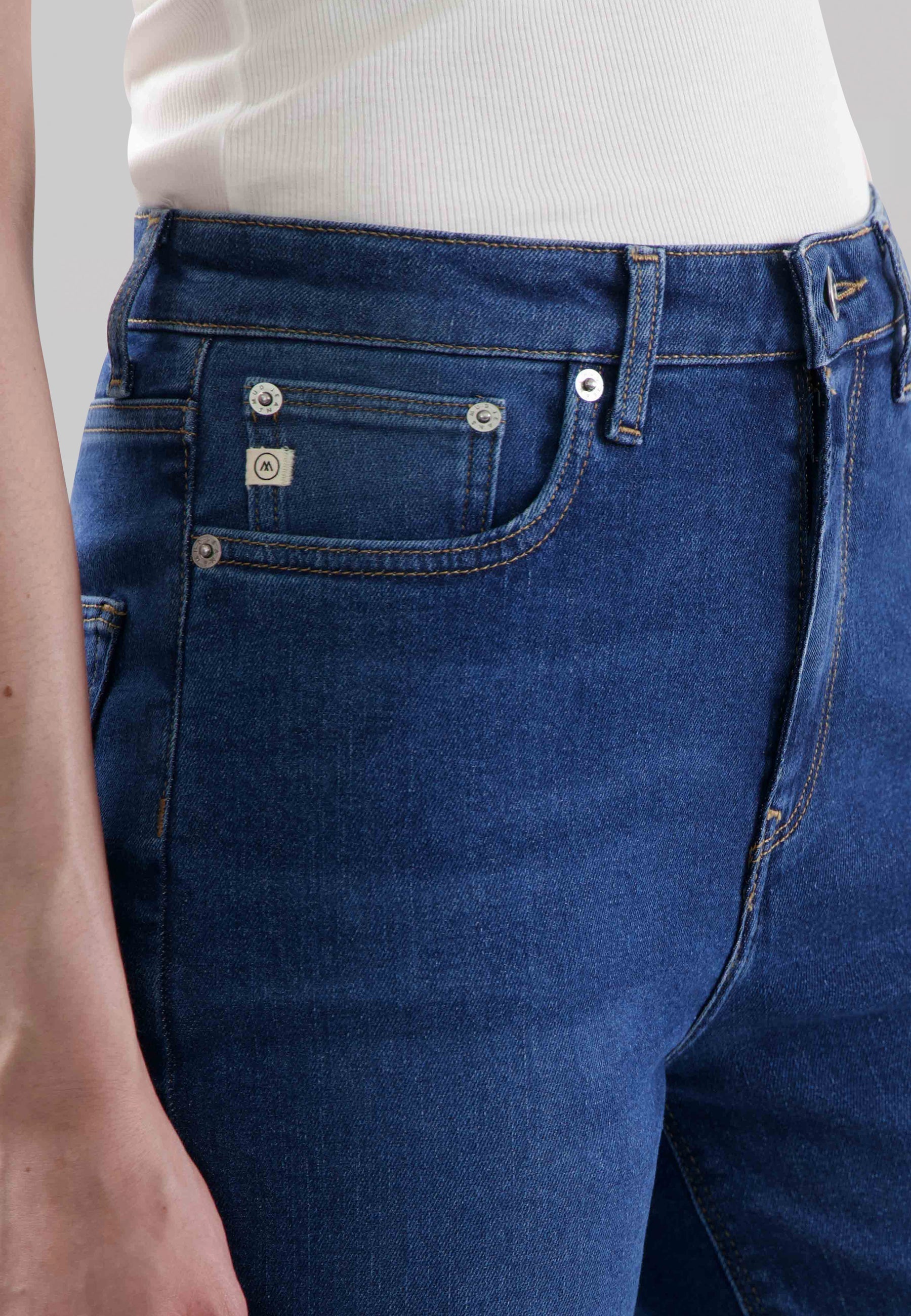 Dark blue denim jeans featuring front pockets and silver button details, worn with a white ribbed sleeveless top.