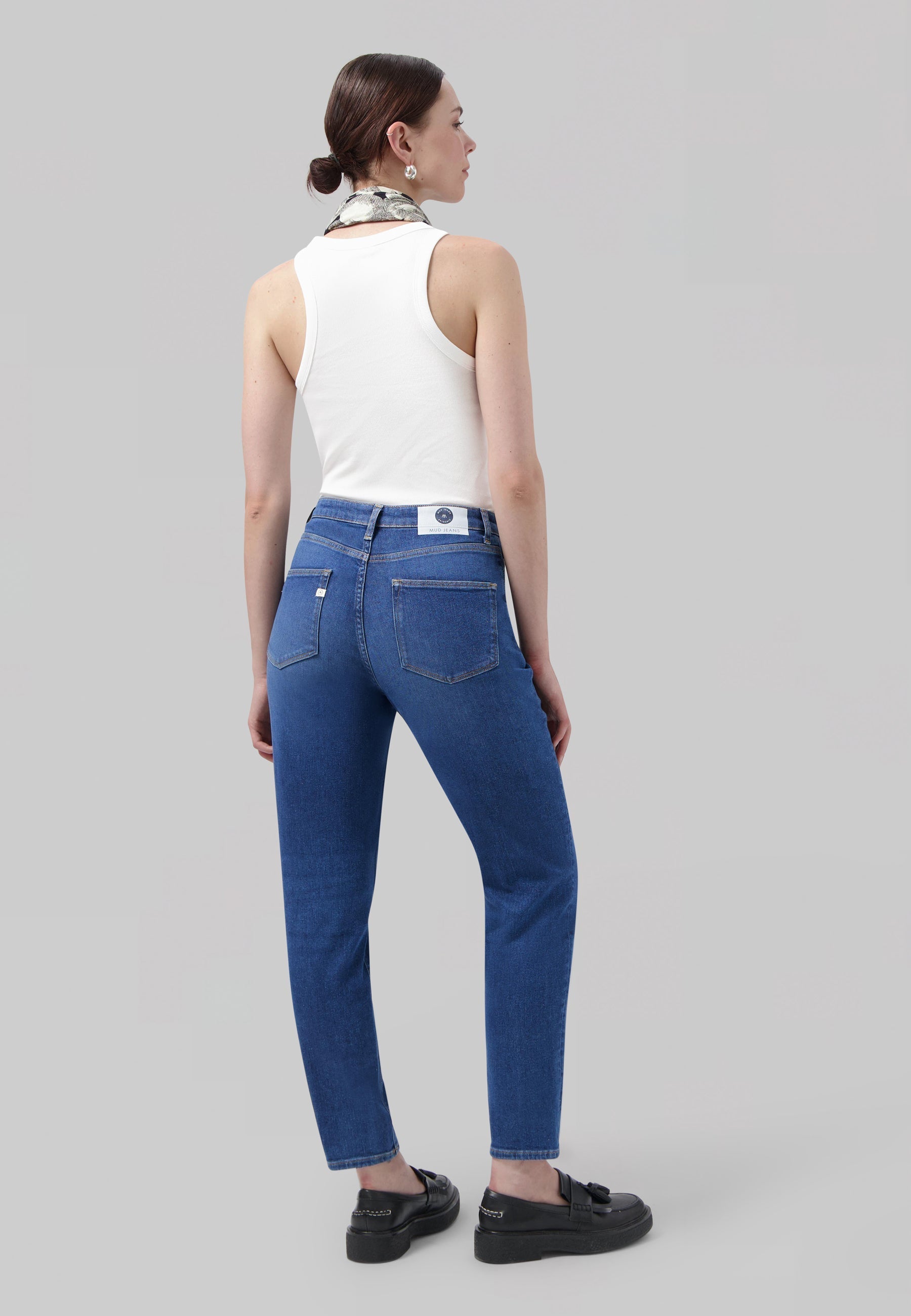 Casual blue denim jeans paired with a white sleeveless top and loafers, styled with a chic scarf accessory.