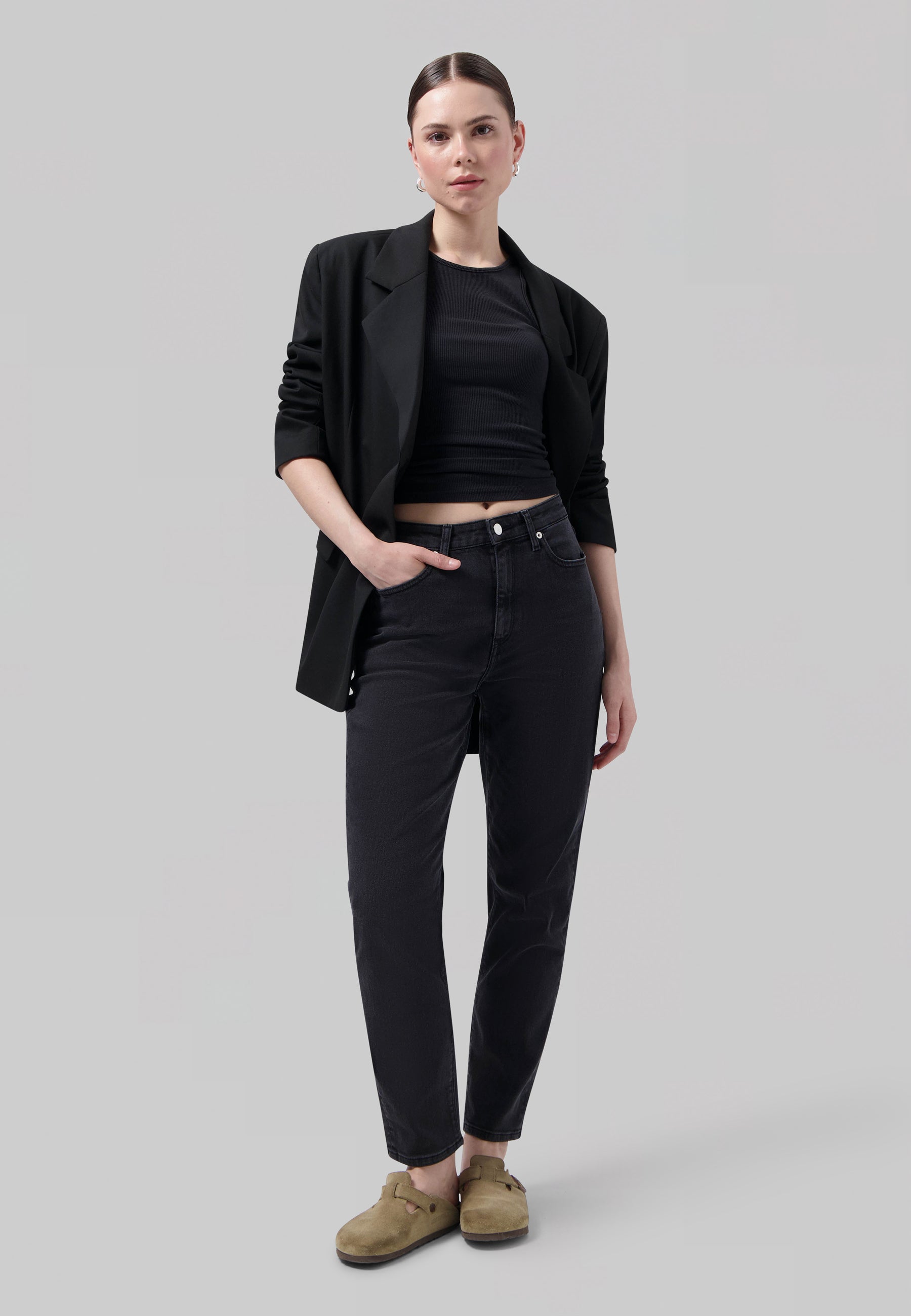 Woman wearing a black blazer over a fitted black top, paired with dark high-waisted jeans and casual tan slip-on shoes.