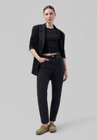 Woman wearing a black blazer over a fitted black top, paired with dark high-waisted jeans and casual tan slip-on shoes.