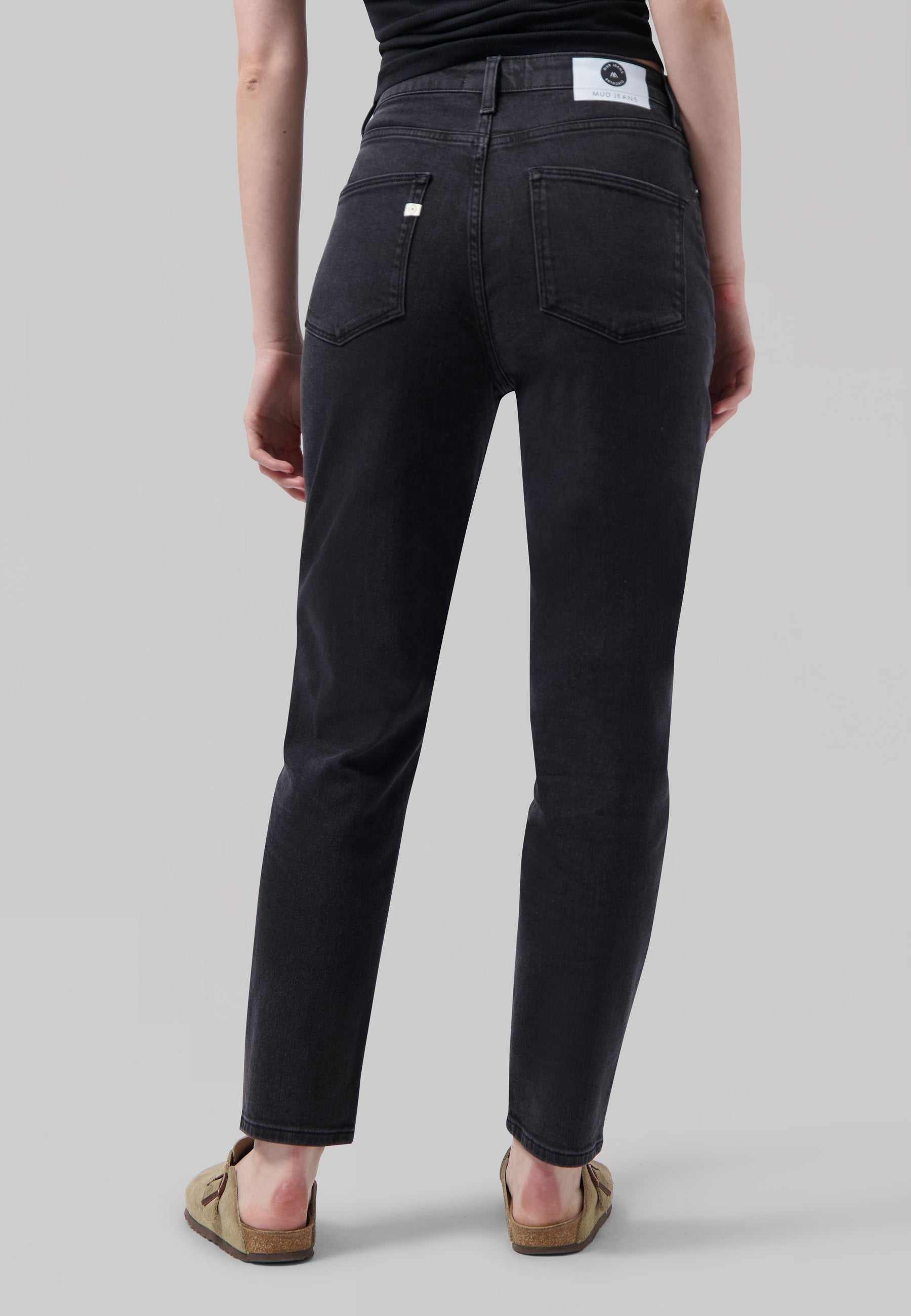 Dark gray MUD Jeans made from sustainable cotton, showcasing a high-waisted, slim-fit design worn with a black top.