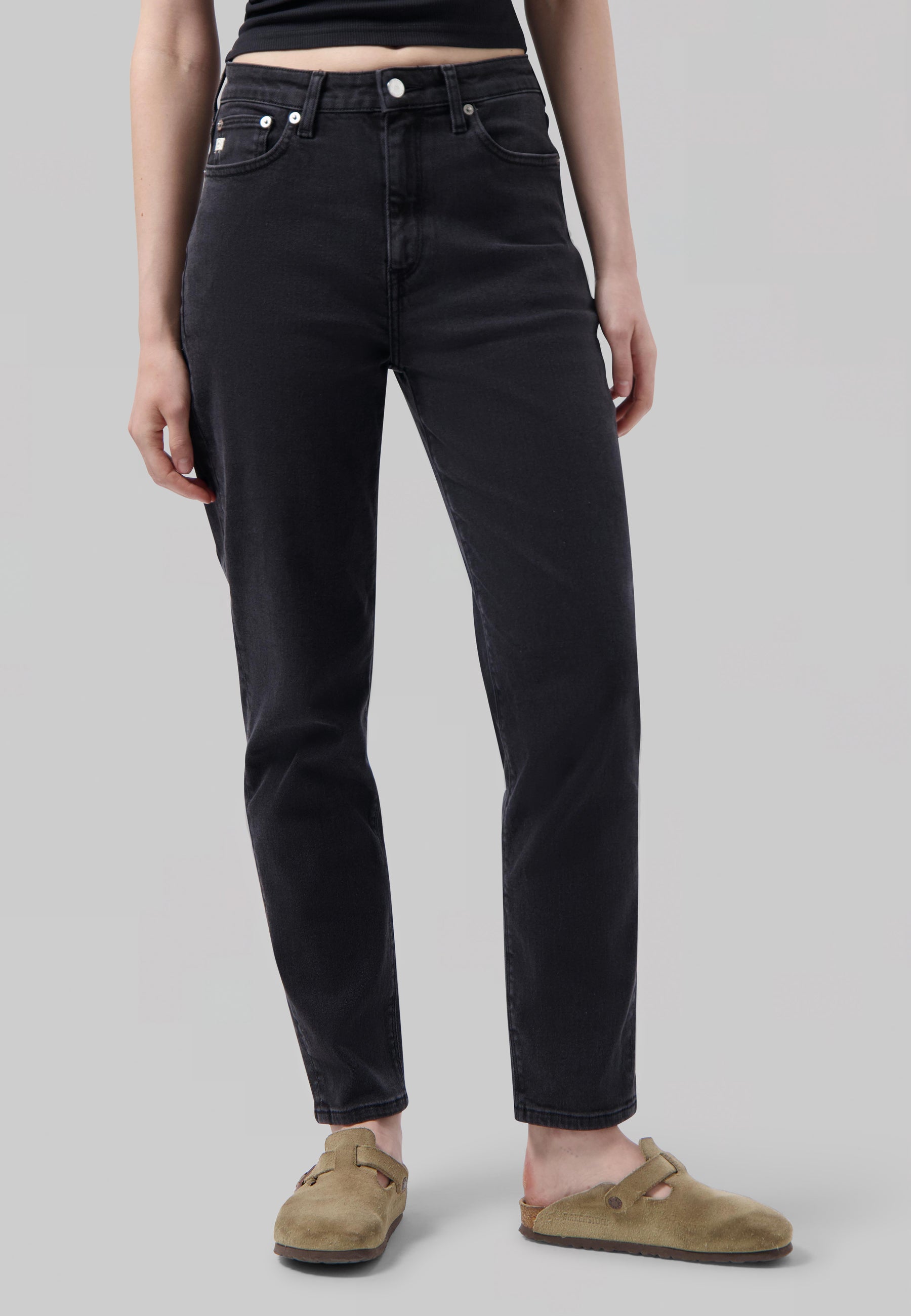 Ankle-length, black slim-fit jeans paired with a black tank top, featuring casual tan suede clogs.