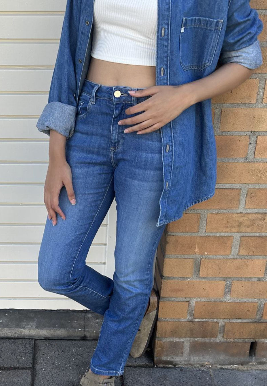 Casual denim outfit featuring blue jeans and a denim shirt paired with a white ribbed crop top for a relaxed style.