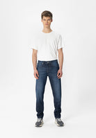 Sustainable MUD Jeans blue denim jacket made from ethical materials, worn with white top and beige pants.