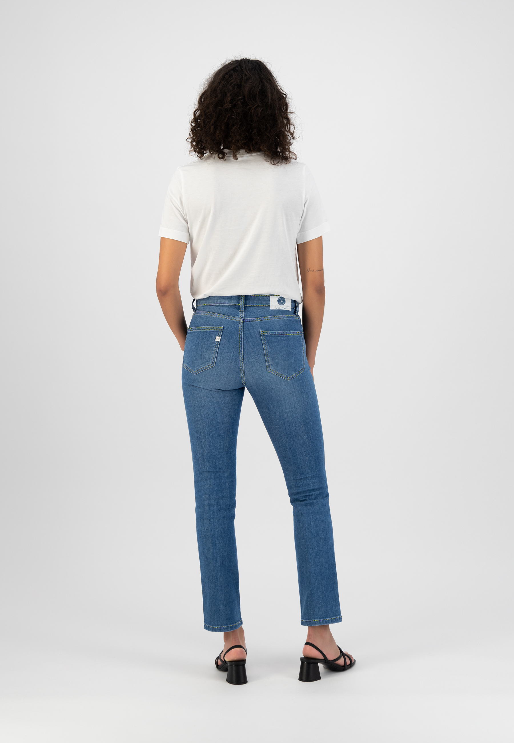 Back view of woman wearing blue straight-leg jeans with white short-sleeve top and black heeled sandals.