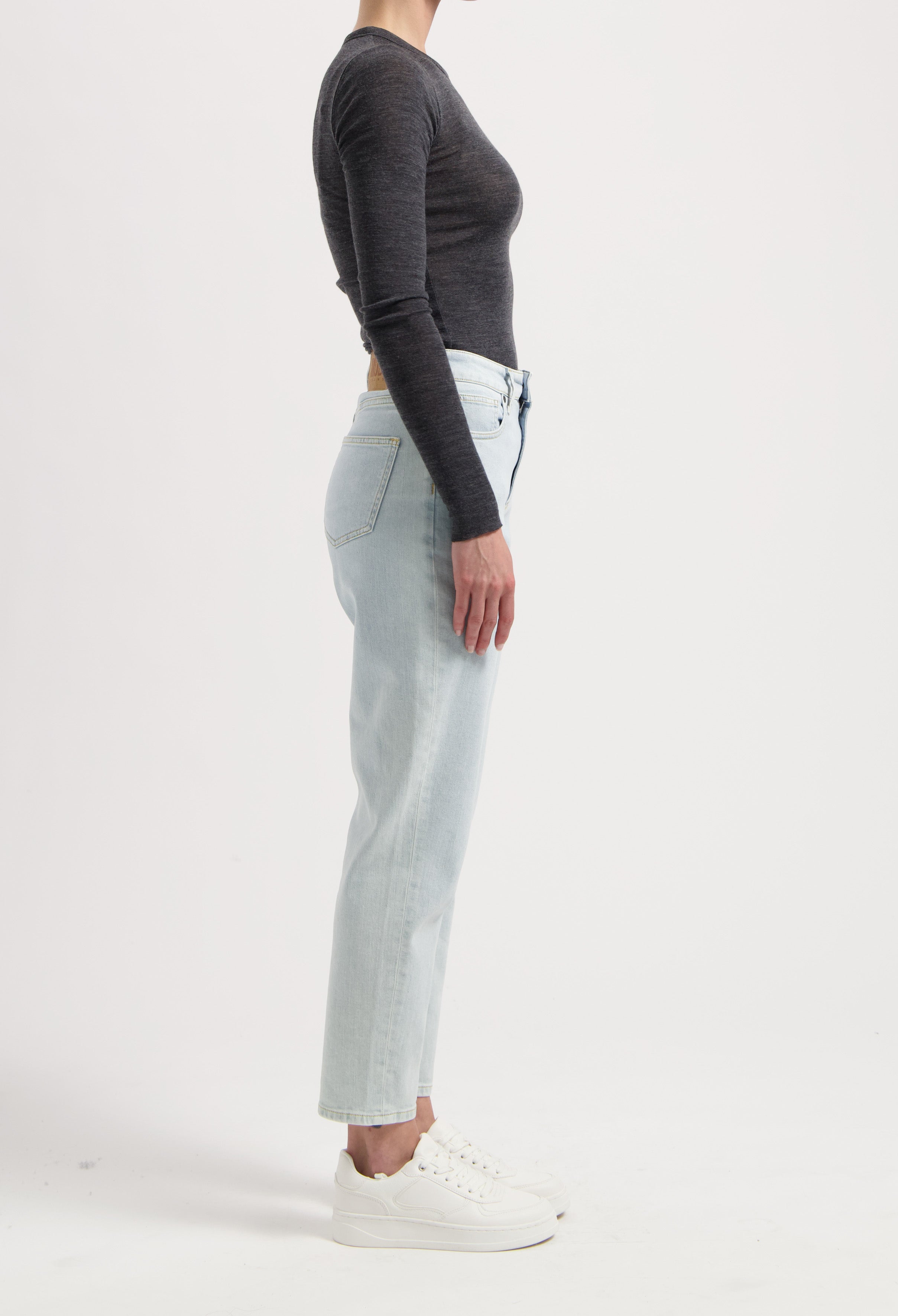 Side profile of a person wearing light wash, high-waisted jeans with a dark gray long-sleeve top and white sneakers.