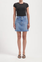 Woman wearing a light blue denim skirt paired with a fitted black short-sleeve top, showcasing casual chic style.