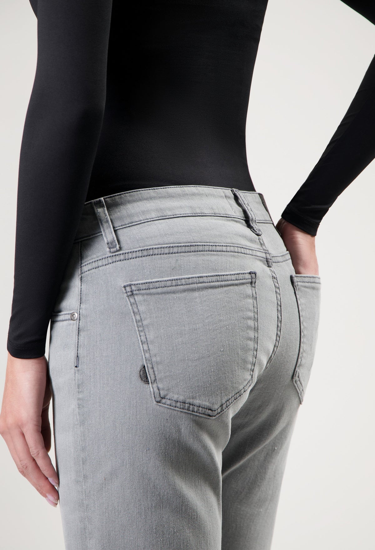 Person wearing light gray jeans with back pockets, styled with a black long-sleeve top, showcasing casual fashion.