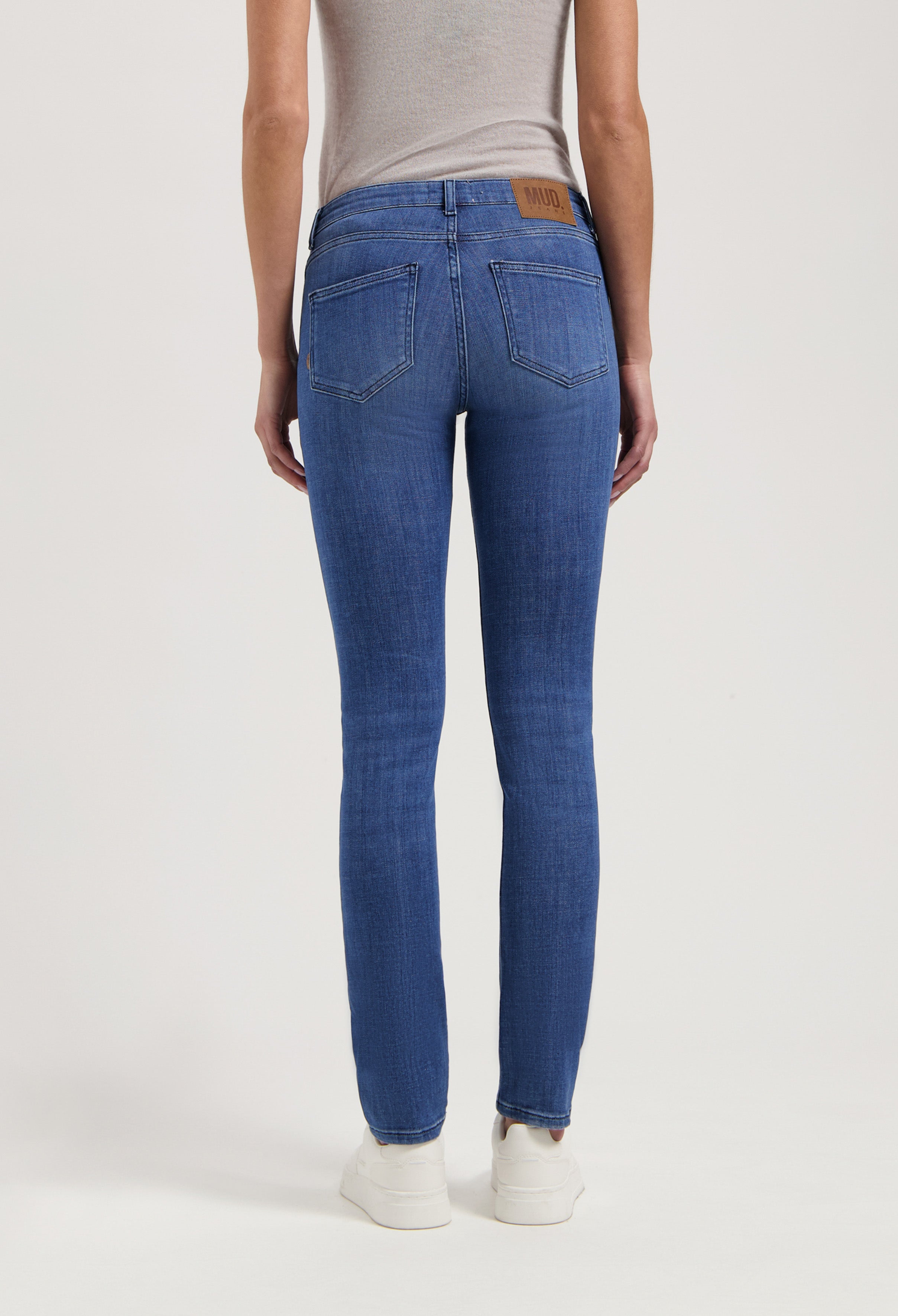 Back view of blue denim slim-fit jeans by MUD Jeans, made from organic cotton, paired with a light gray sleeveless top.