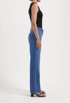 Woman wearing fitted blue jeans and a sleeveless black top, showcasing casual style with strappy black heels.