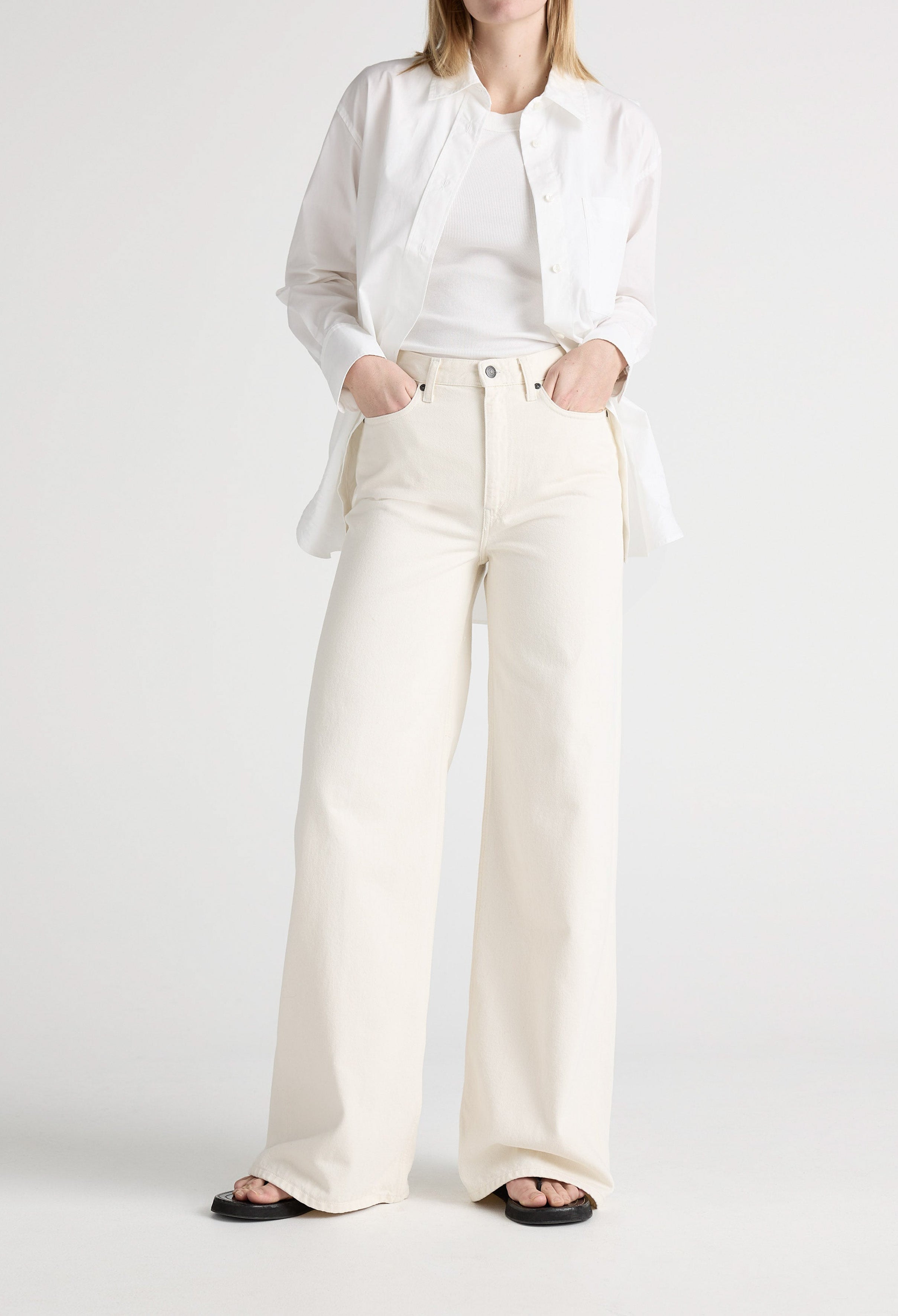 White wide-leg denim jeans paired with a tucked-in white tank top and unbuttoned shirt, worn with black sandals.