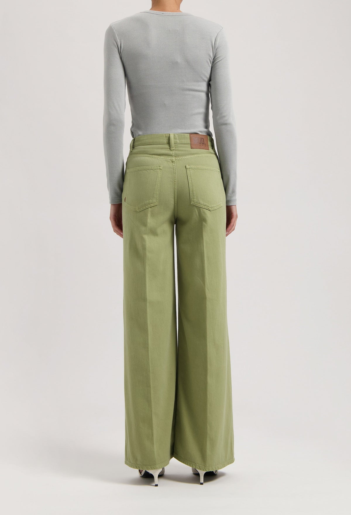 High-waisted, wide-leg MUD Jeans in light green organic cotton worn with a fitted gray long-sleeve top.