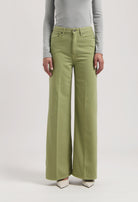 Green wide-leg jeans made from cotton, worn with a light gray long-sleeve top, showcasing a stylish casual look.
