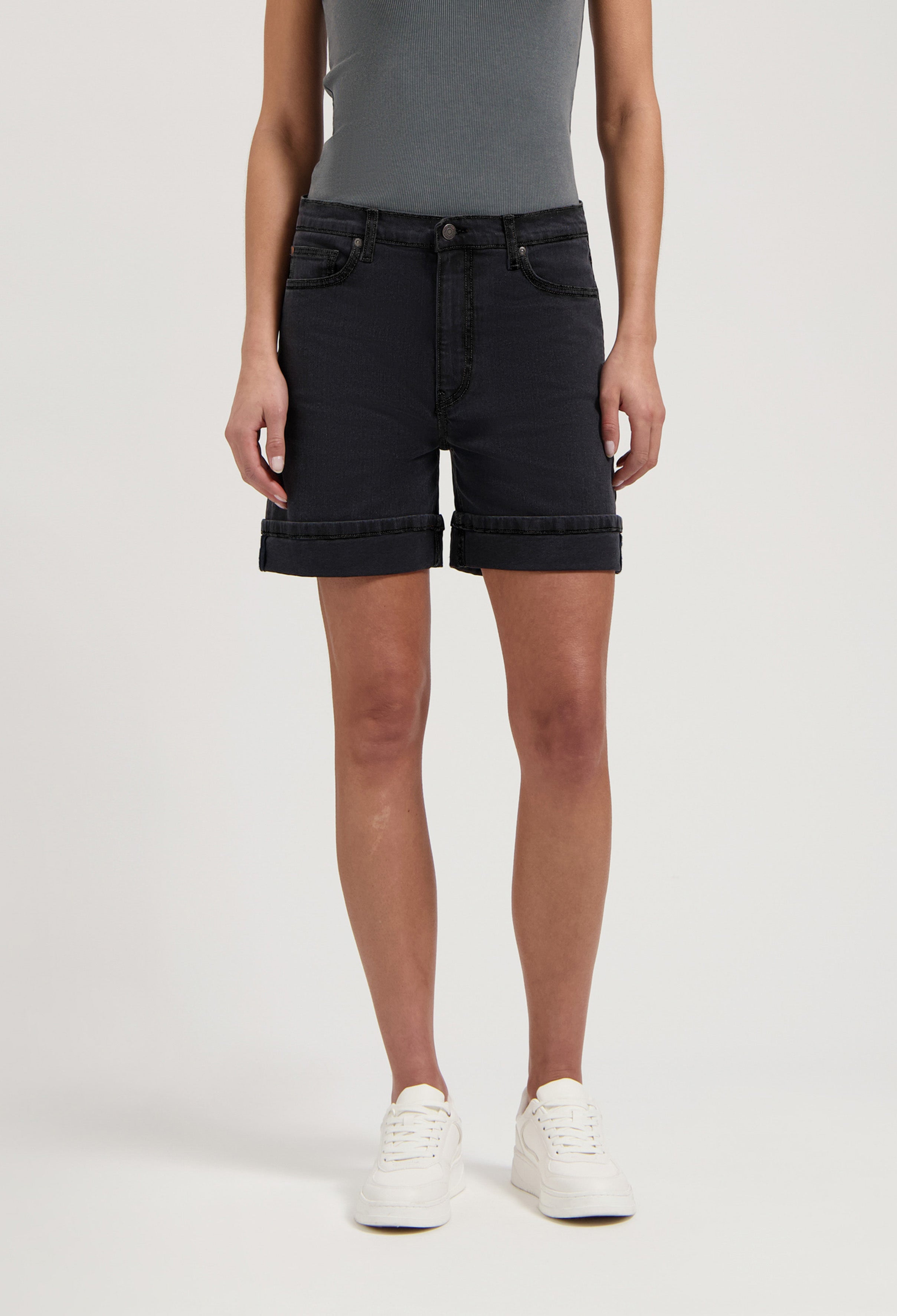 Black denim shorts paired with a sleeveless gray top and white sneakers, highlighting casual summer fashion.