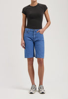 Casual light blue denim Bermuda shorts paired with a fitted black tee and gray sneakers, showcasing a relaxed outfit.