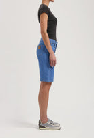 Side view of a woman wearing a black fitted t-shirt paired with blue knee-length denim shorts and gray sneakers.