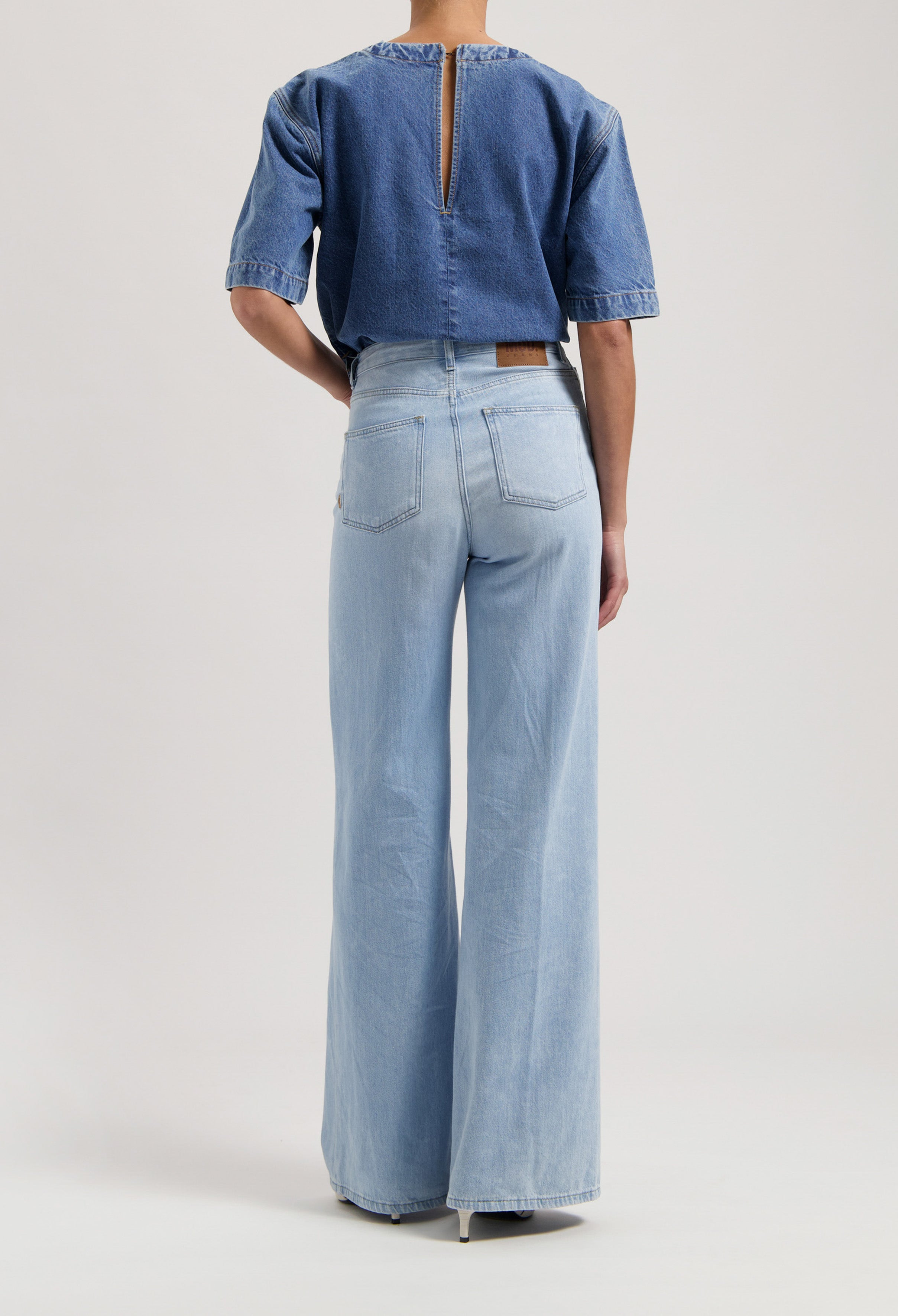 A denim ensemble with a back zipper blue top and light blue, wide-leg jeans, showcasing sustainable fashion.