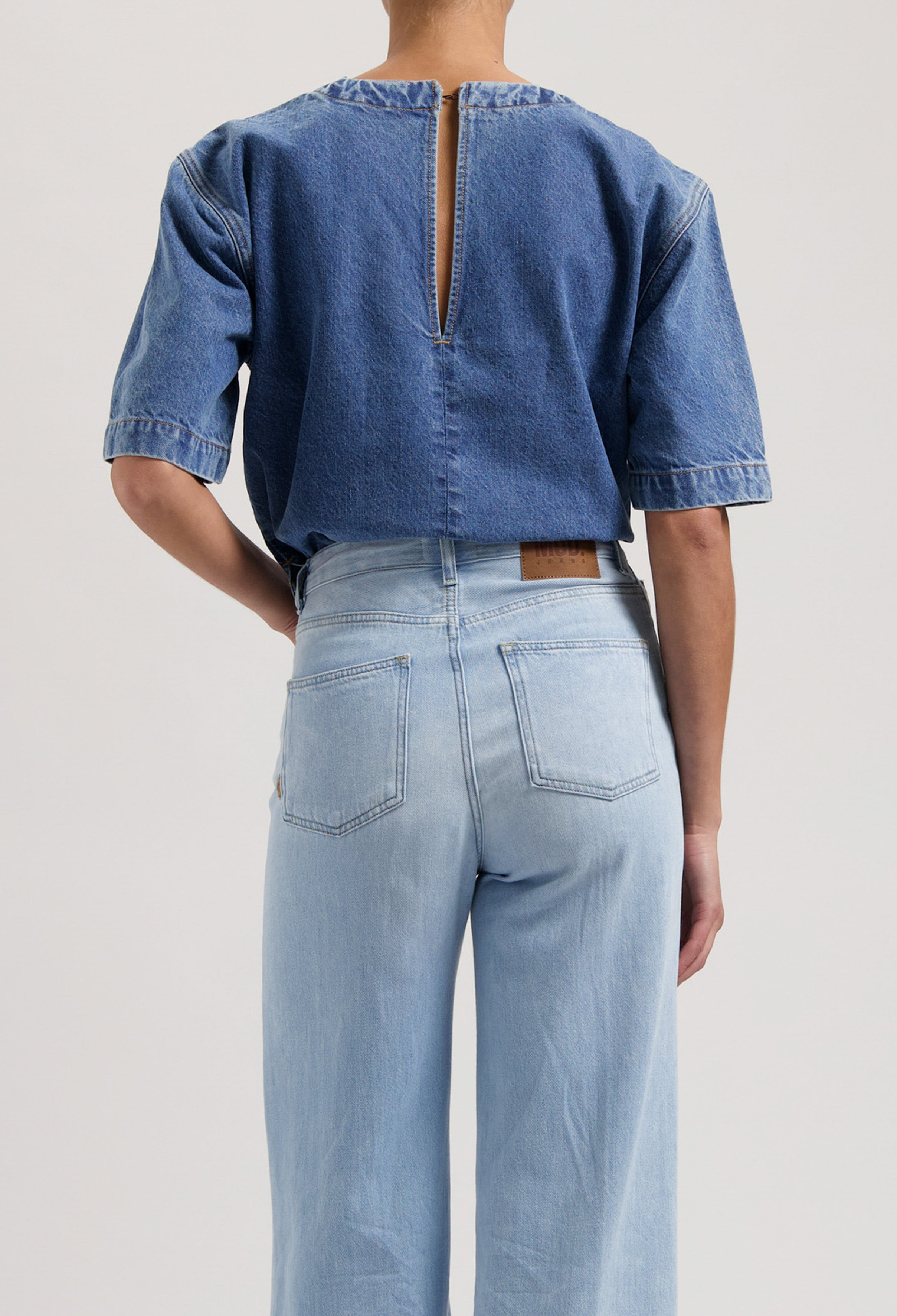Back view of a model wearing a casual blue denim top and high-waisted light wash jeans, showcasing sustainable fashion.